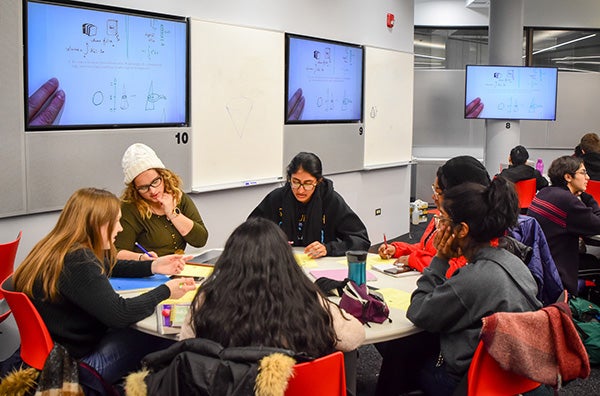 UIC students work in a classroom equipped with large presentation screens around the room.